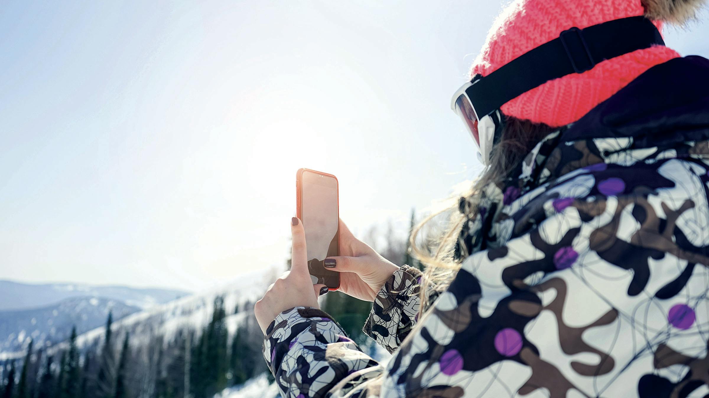 Woman in ski gear holding up phone to take a photo in the mountains