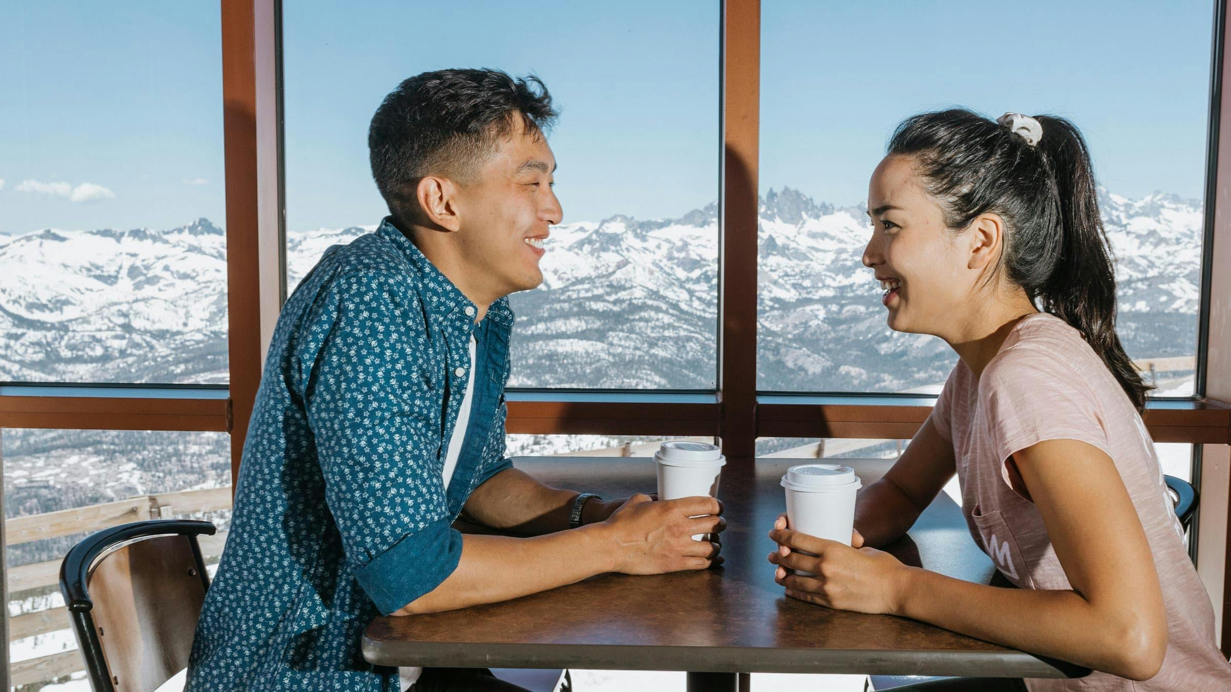 Man and woman drinking coffees inside Eleven53 Café with a view of the mountains outside the window
