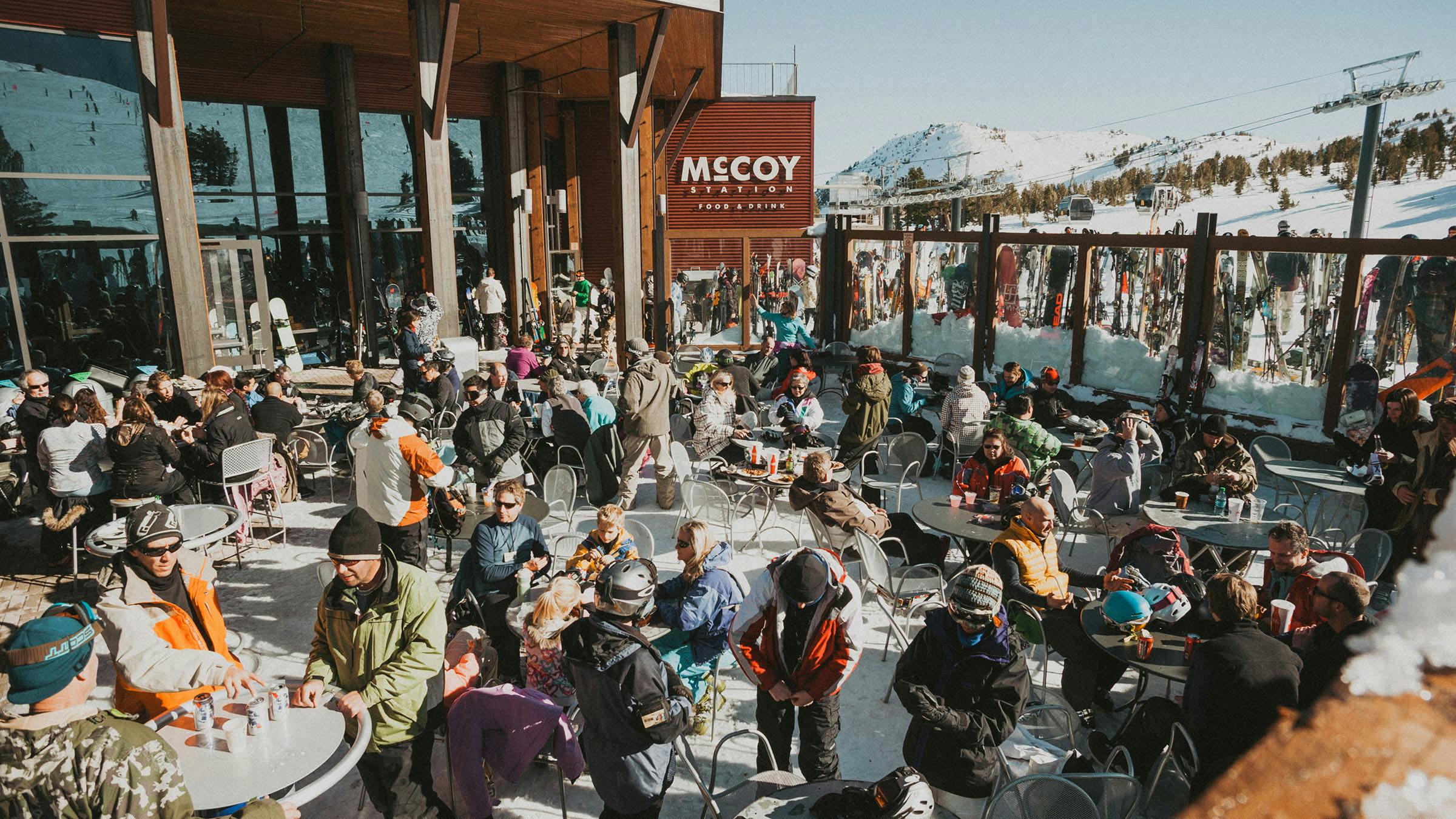 People at tables enjoying drinks outside McCoy Station at Steeps Bar with snowy mountain in the background