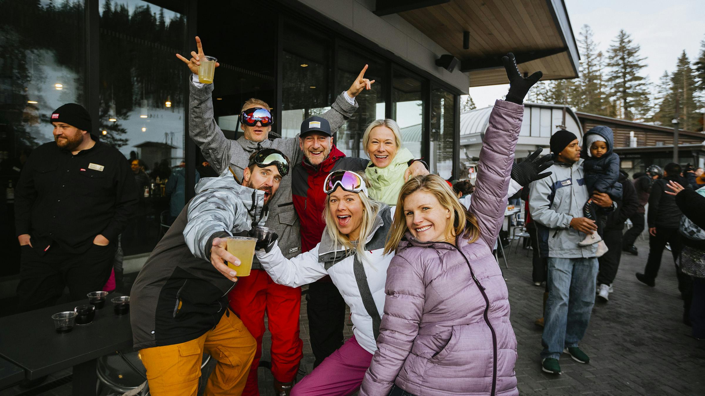 Group of five friends dressed in ski gear holding drinks and posing for a photo with arms up at Weekend Aprés Party at Canyon Lodge
