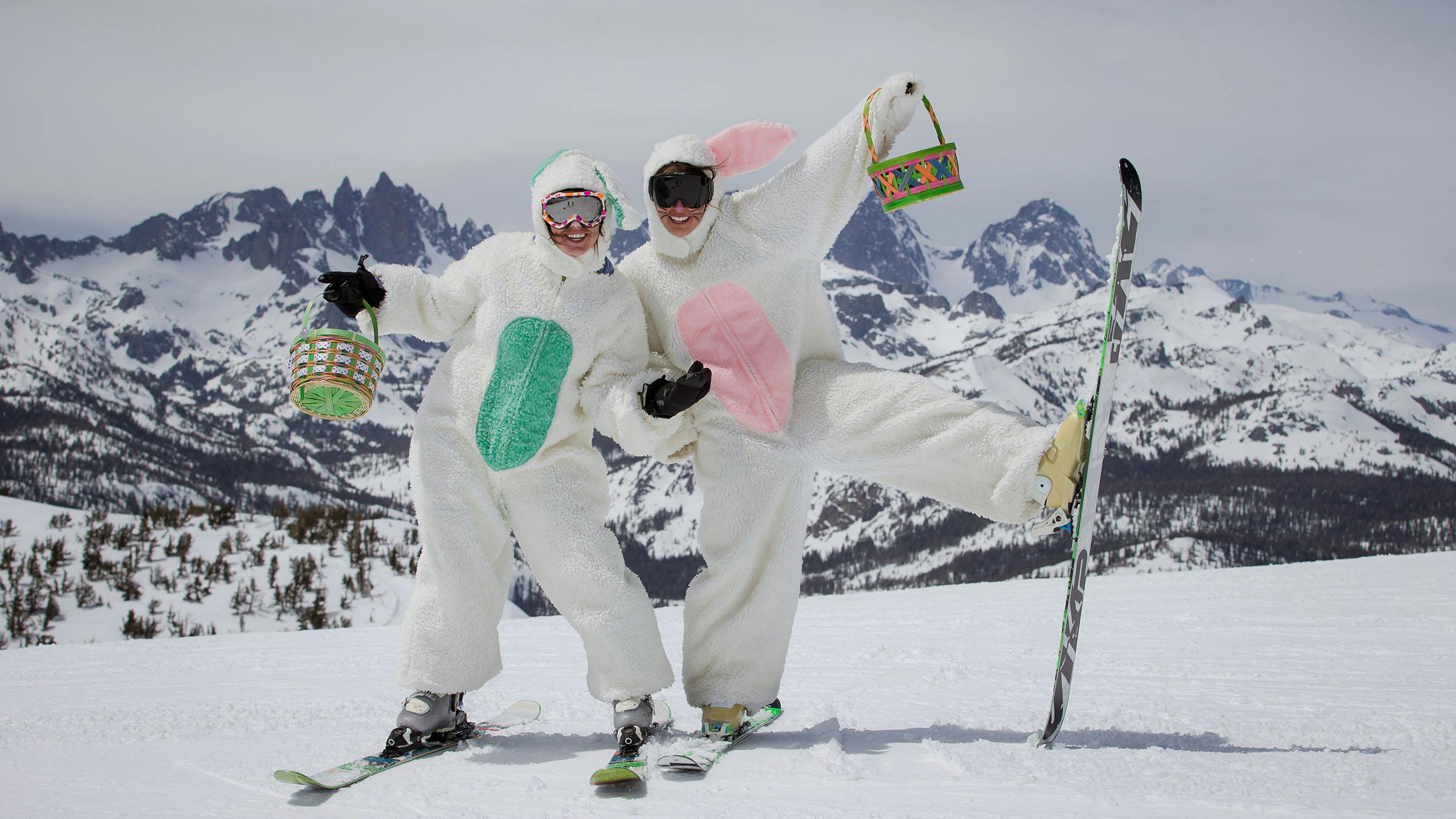 Two Easter Bunnies on skis holding up baskets of eggs on the summit of Mammoth Mountain