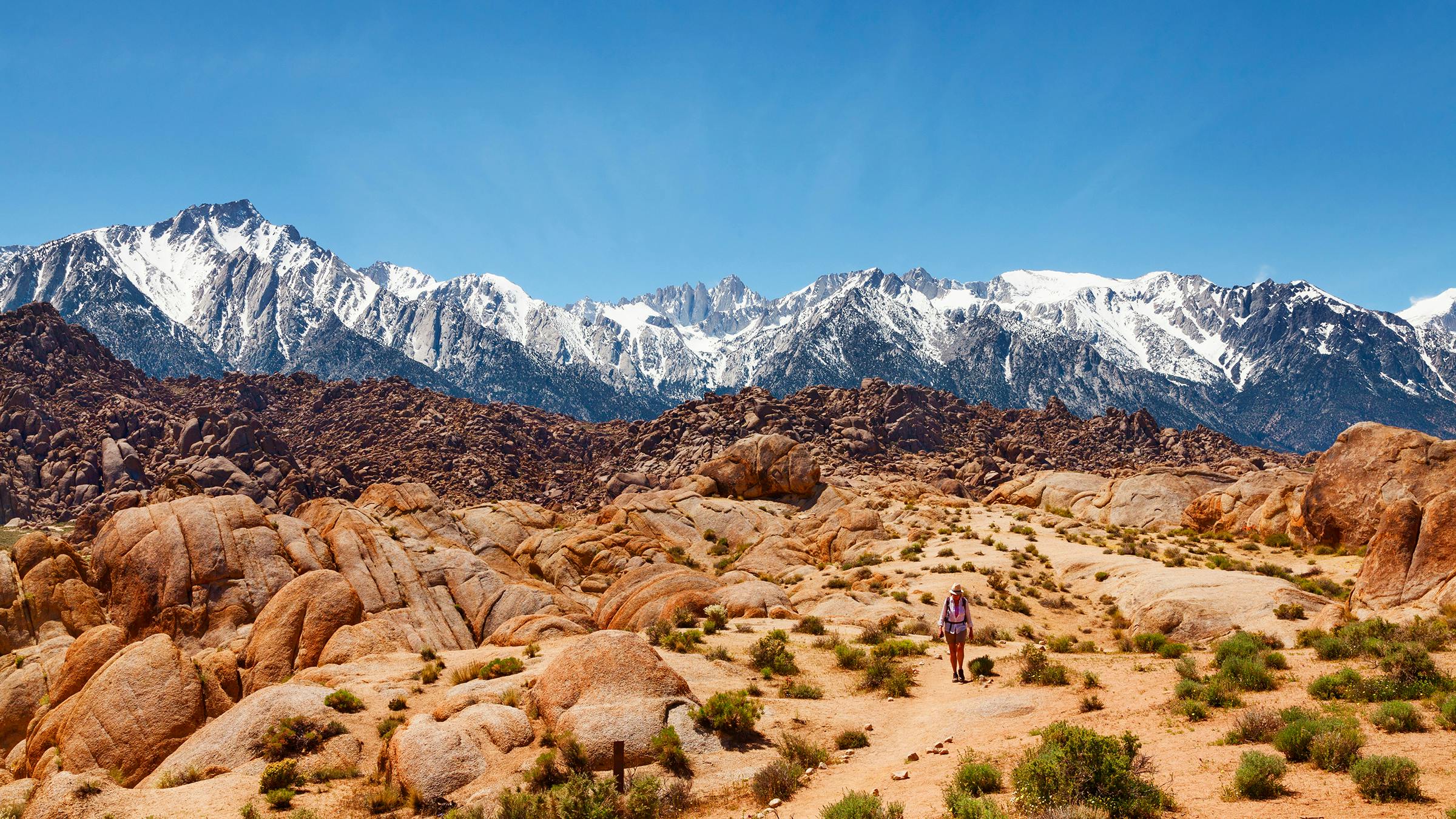 Tan rock formations in Alabama Hills with blue sky and snow-covered mountains in background
