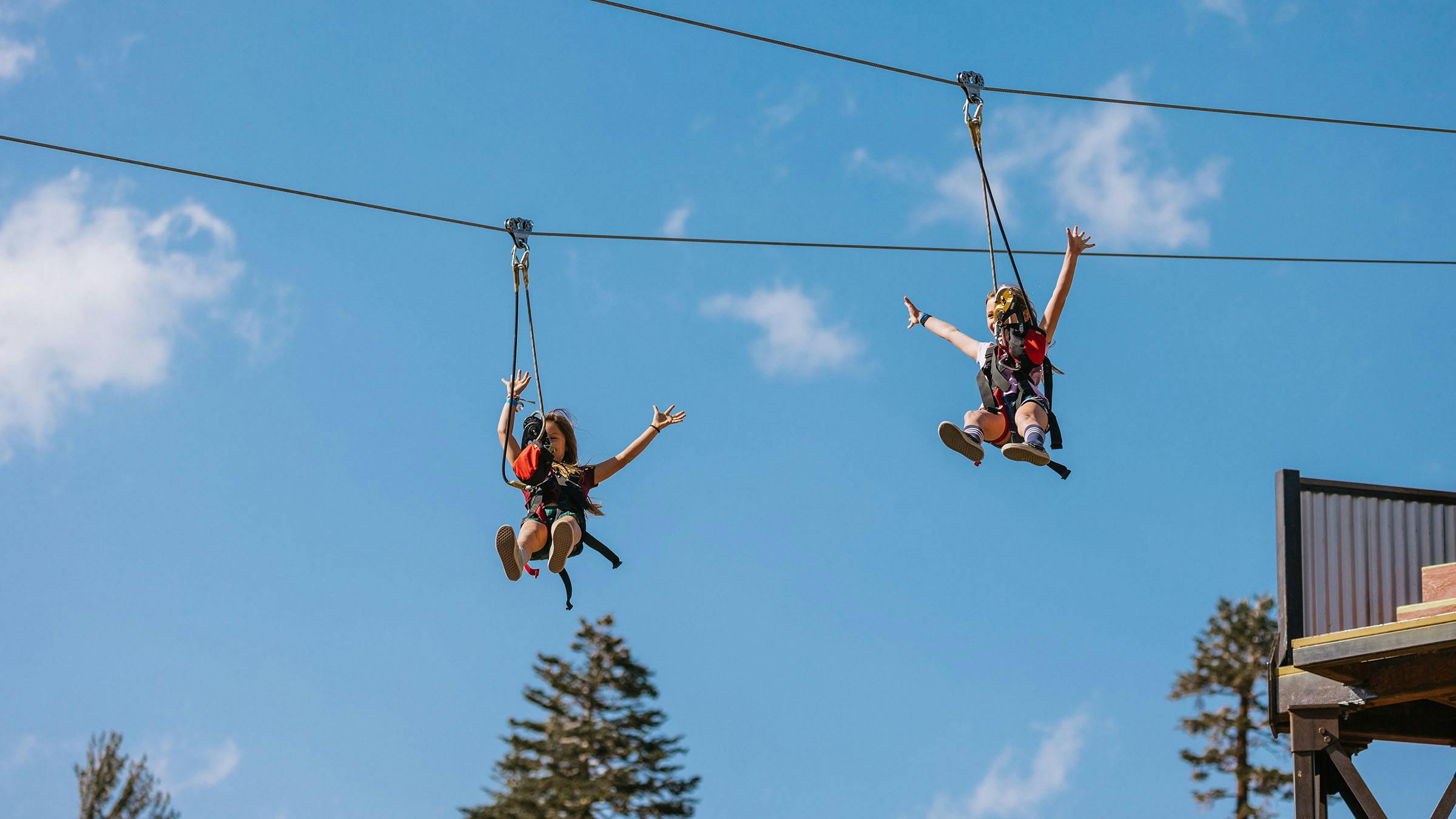 Two girls with hands in the air on zip line 
