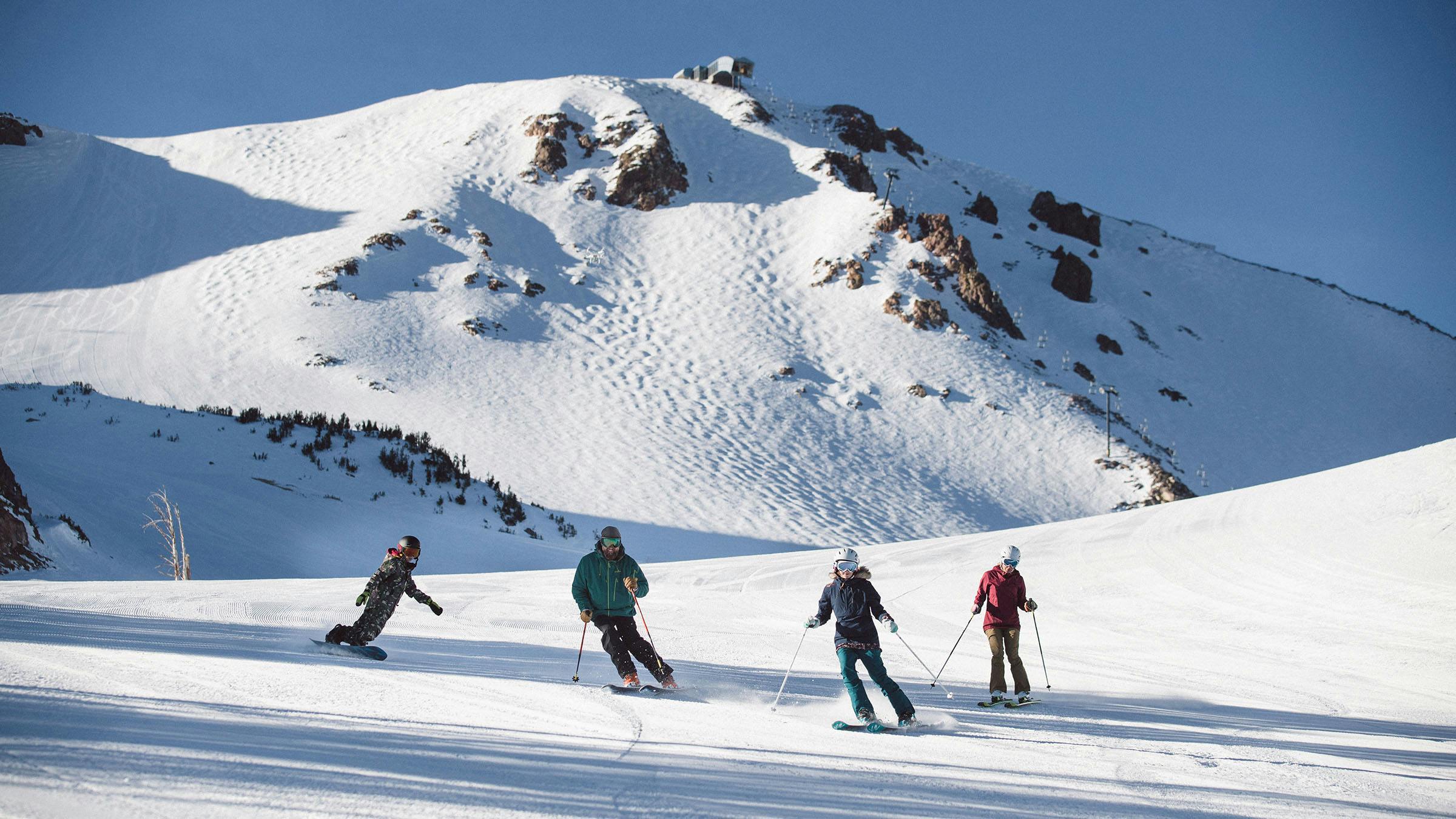 4 skiers on a bluebird day enjoying morning groomers with Mammoth Mountain in background