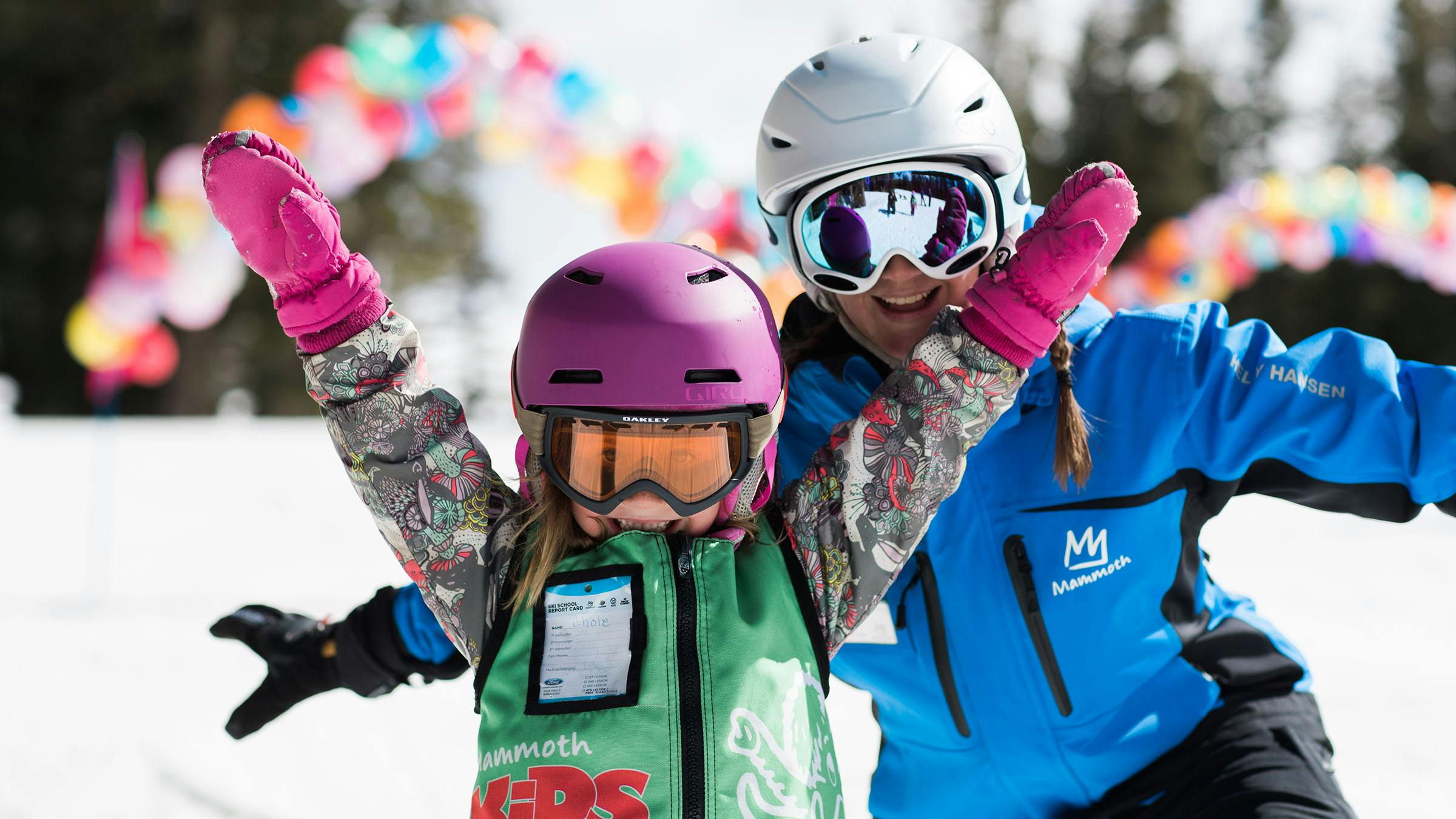 Girl with hands up skiing in front of instructor