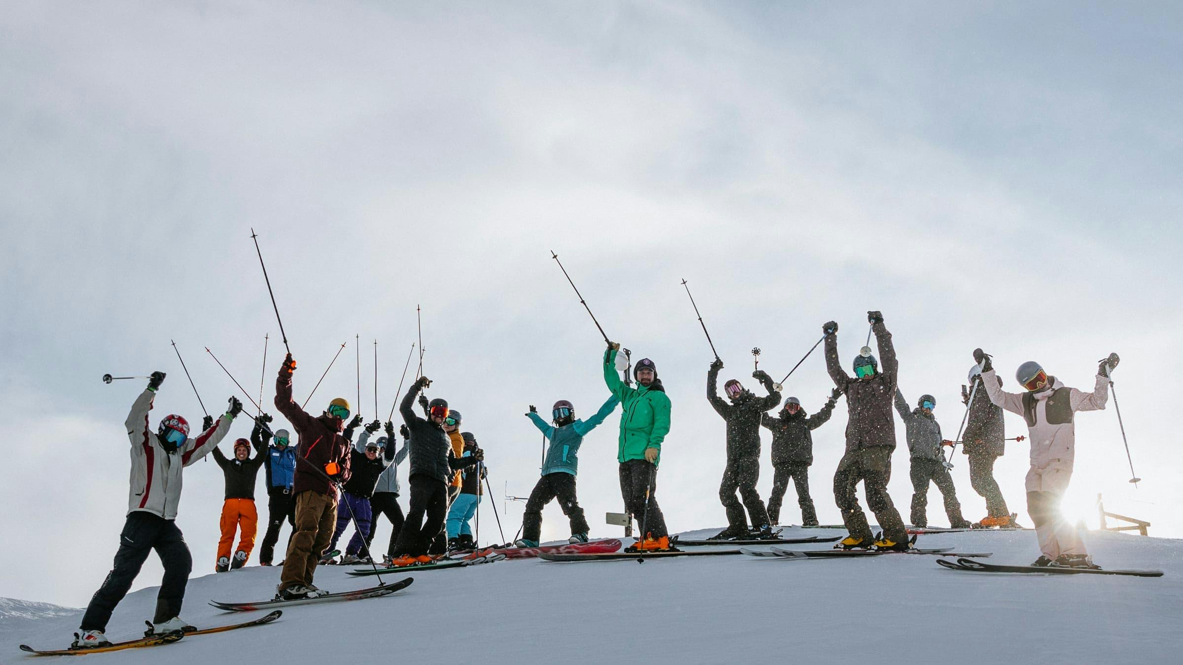 Group of skiers on the hill posing with their hands up for photo