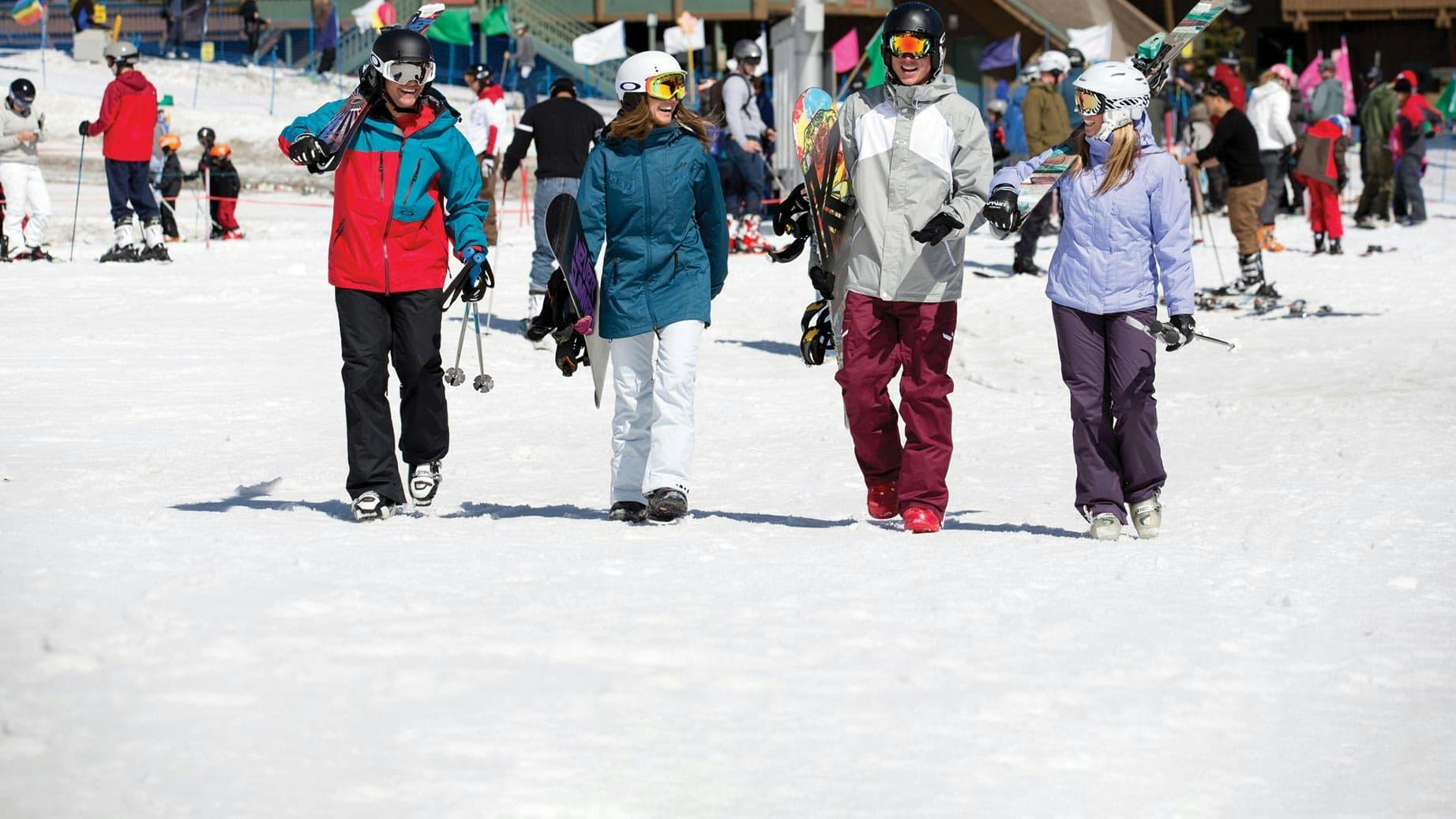 Group of friends carrying their ski and snowboard equipment