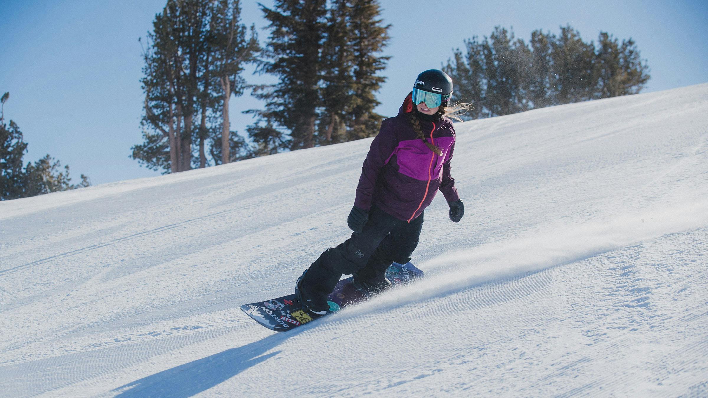 Woman in purple jacket snowboarding morning groomers