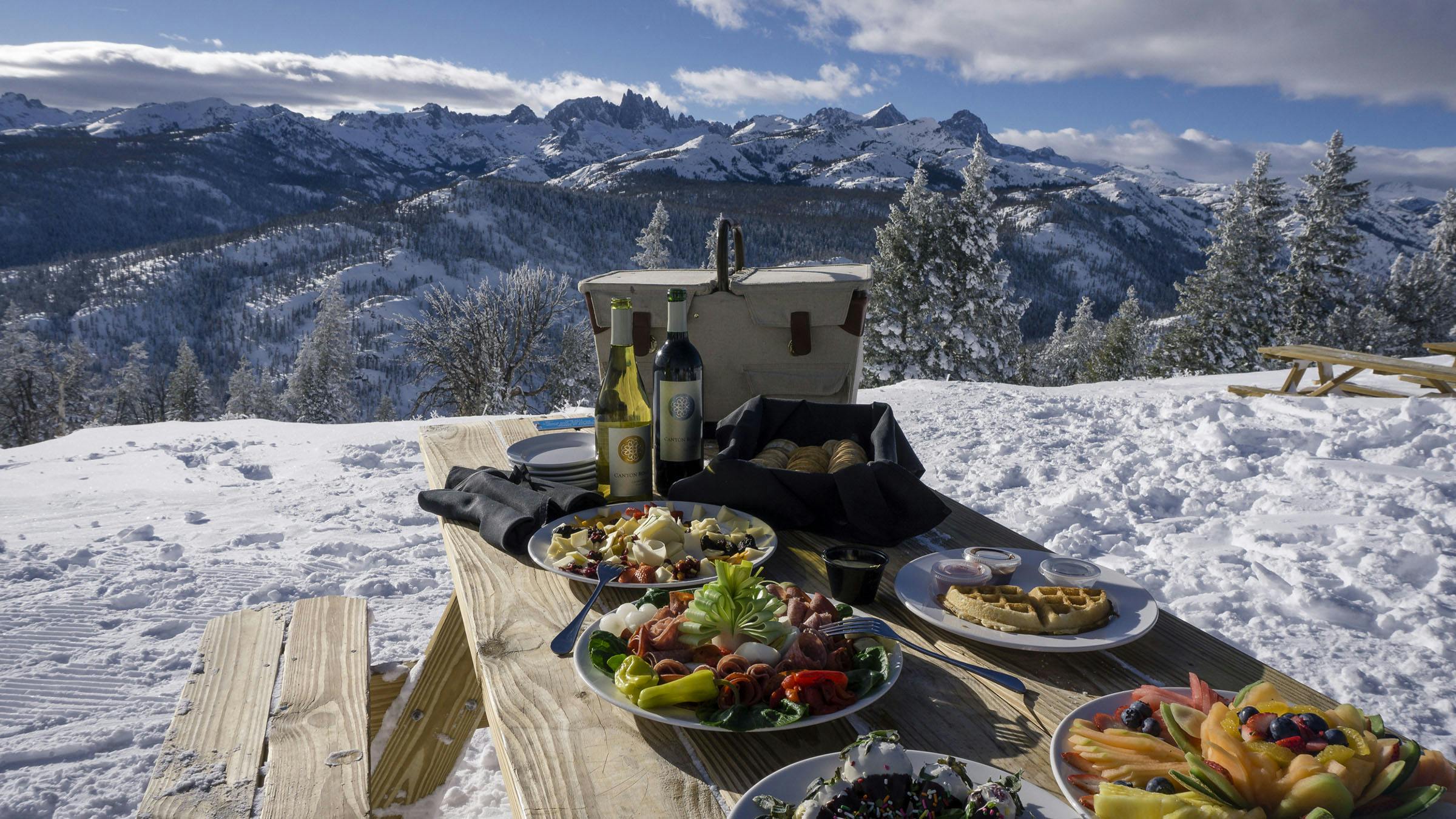 Charcuterie spread on a picnic table at scenic Minaret Vista with snowy mountains in the background